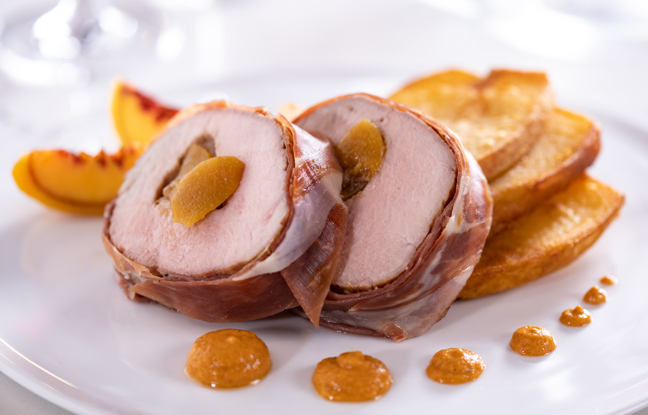 Peach and onion stuffed roasted veal loin wrapped in jamón ibérico served with patatas bravas and romesco coulis